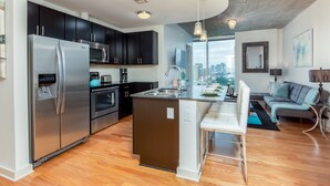 Une cuisine moderne dotée d’appareils électroménagers en acier inoxydable, d’un îlot central et offrant une vue sur la ville grâce à de grandes fenêtres.