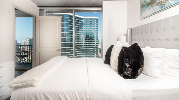 Une chambre avec un grand lit, une vue sur un immeuble de grande hauteur et un balcon avec une chaise.