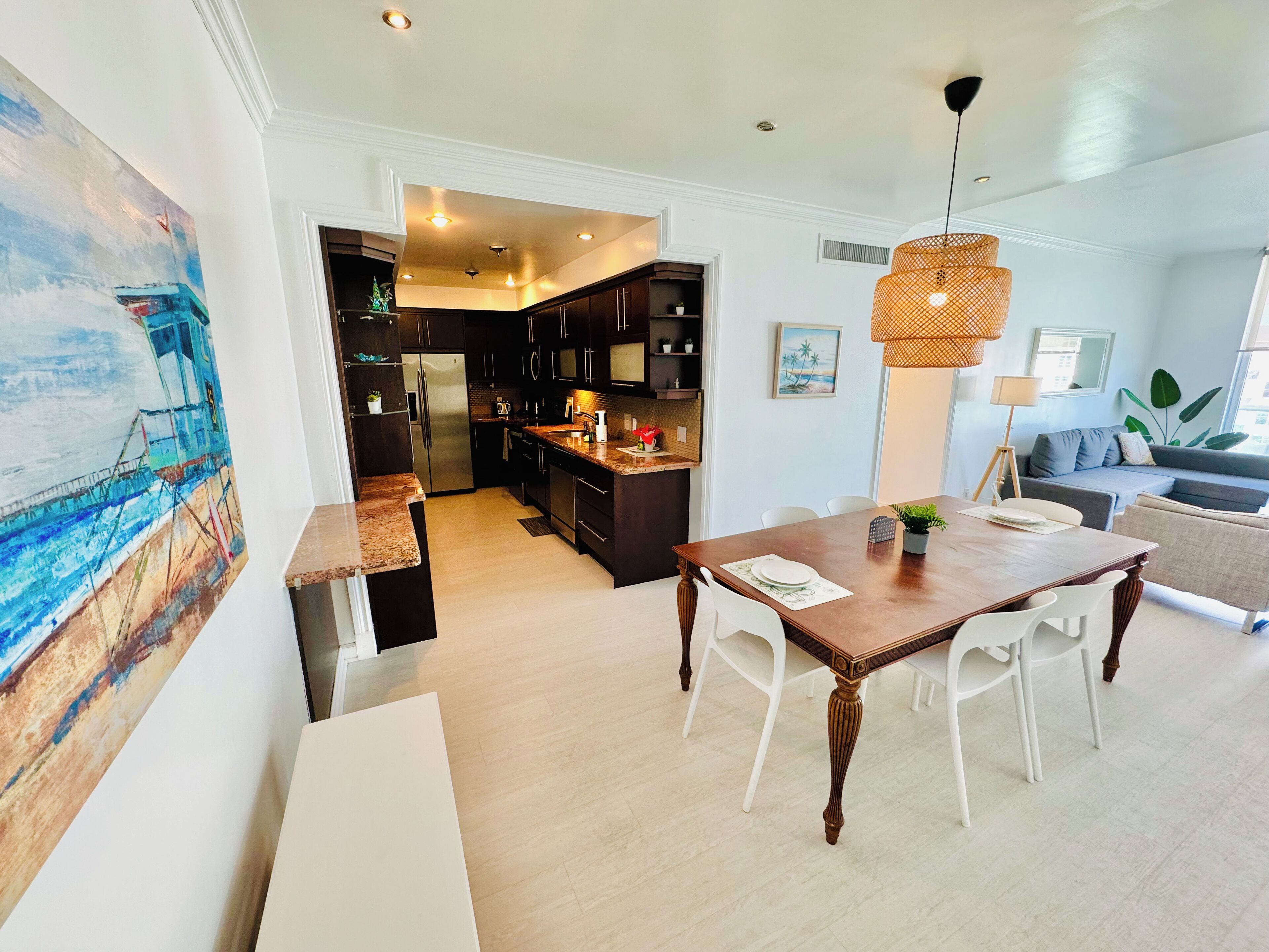 A modern kitchen with dark cabinets, a stainless steel refrigerator, and a dining area with a wooden table and white chairs.