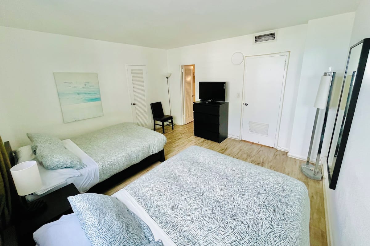 A room with two beds, a desk, a chair, a TV, and a door.