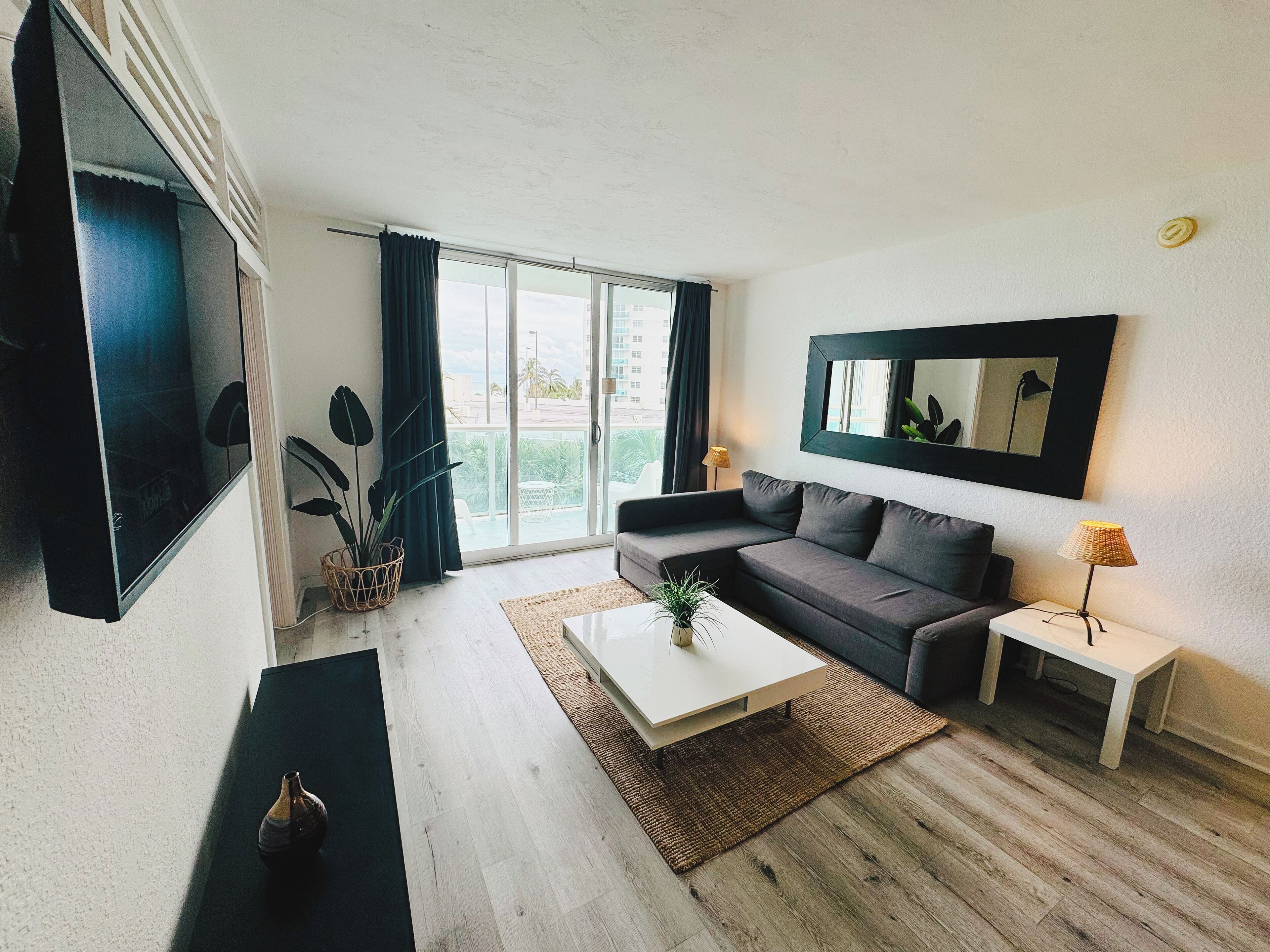 A modern living room with a sofa, a coffee table, a TV, and a large window with curtains.