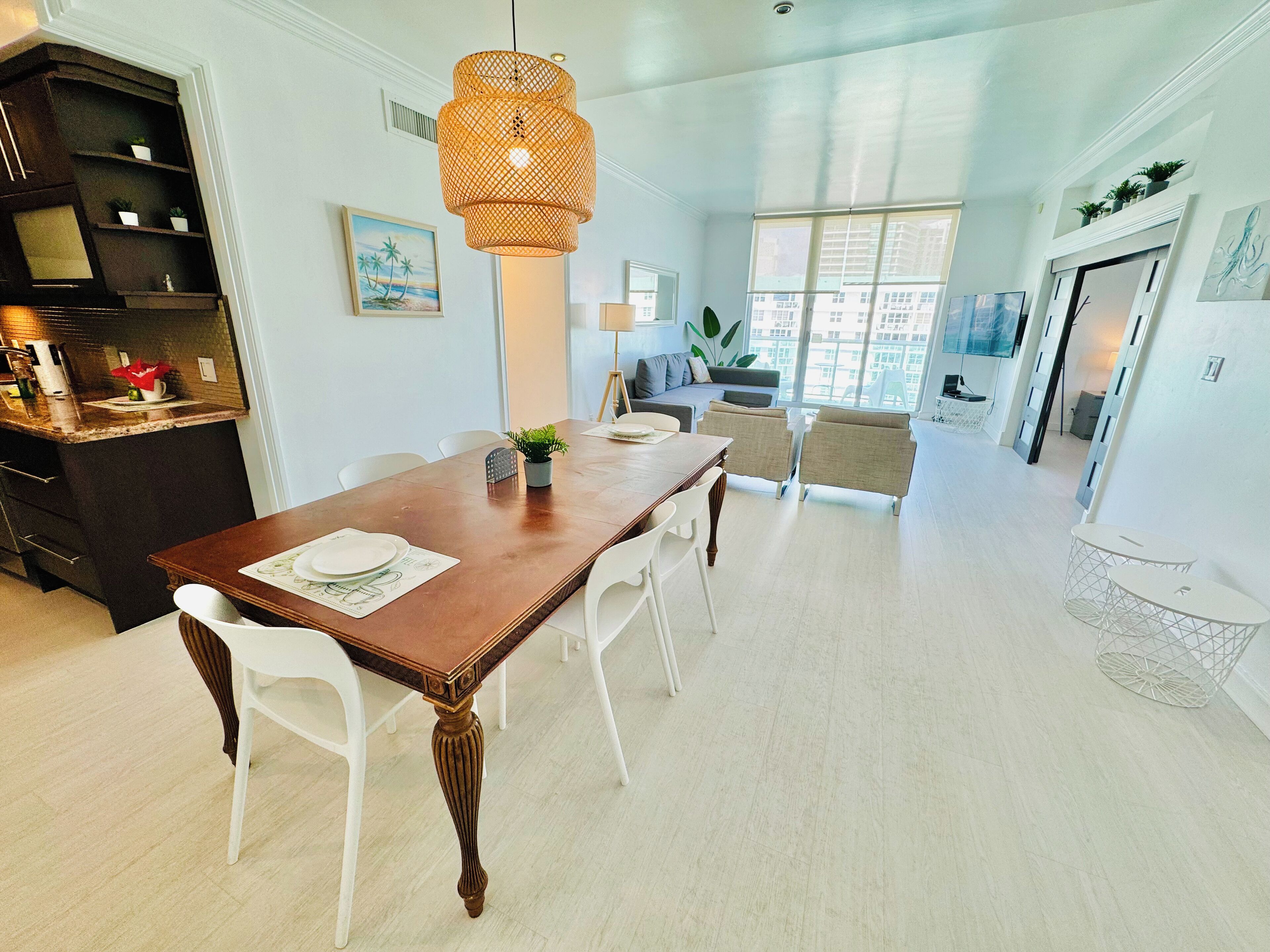A spacious dining area with a wooden table, white chairs, and a hanging light fixture.
