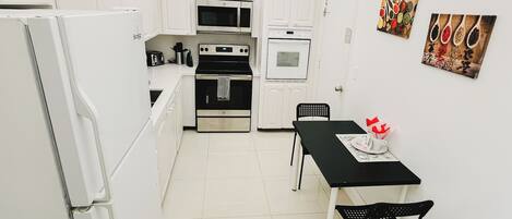 A compact kitchen with white cabinets, a black stove, a microwave, and a table with chairs.