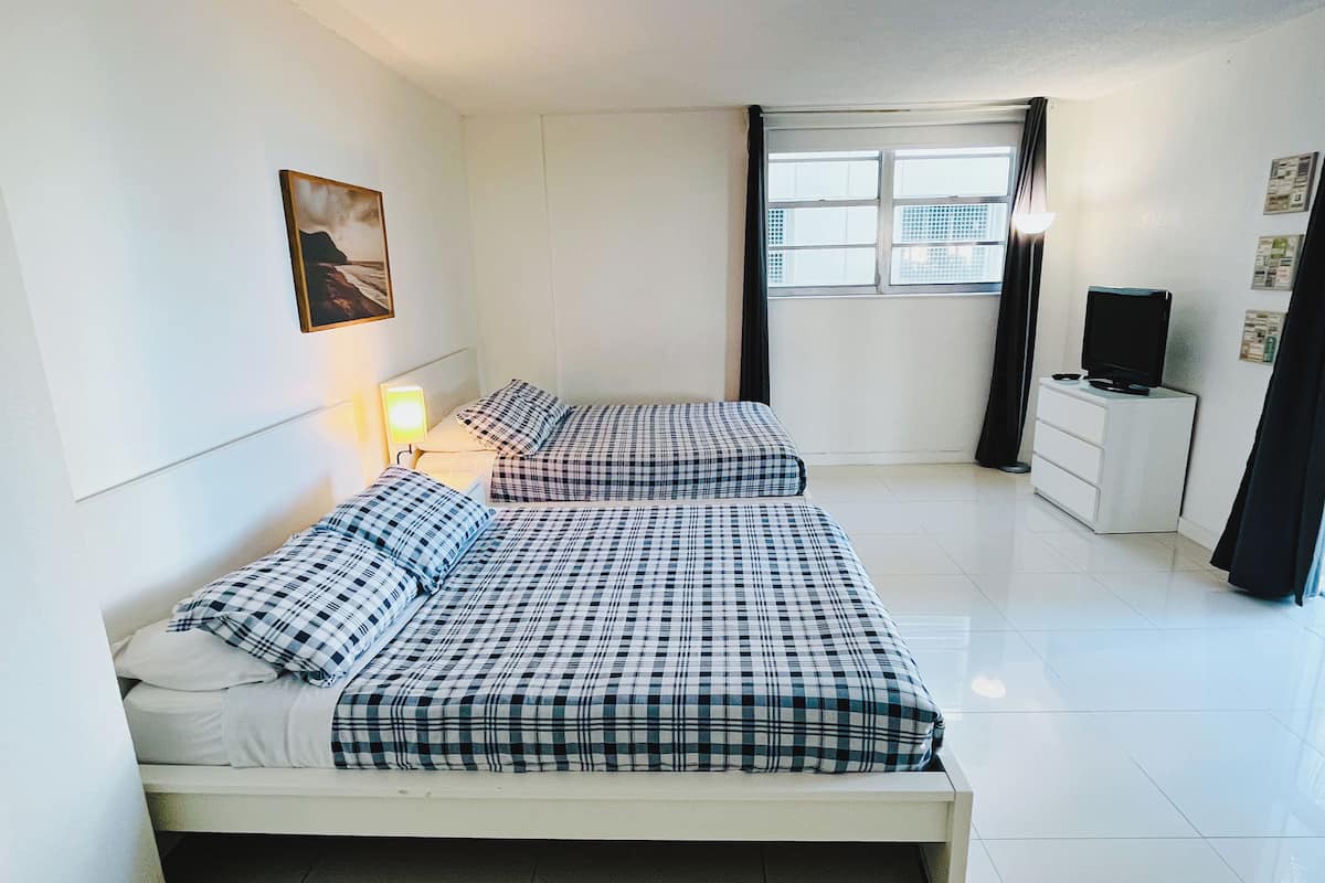 A bedroom with two beds, a nightstand, a TV, and a window with curtains.