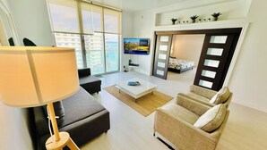 A modern living room with a sofa, a coffee table, and a TV. There is a balcony with a view of the sea. - The Tides on Hollywood (Hollywood)