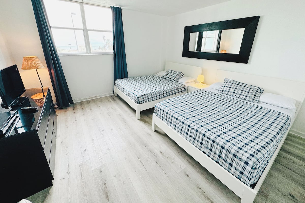 A hotel room with two beds, a TV, a lamp, and a window with curtains.