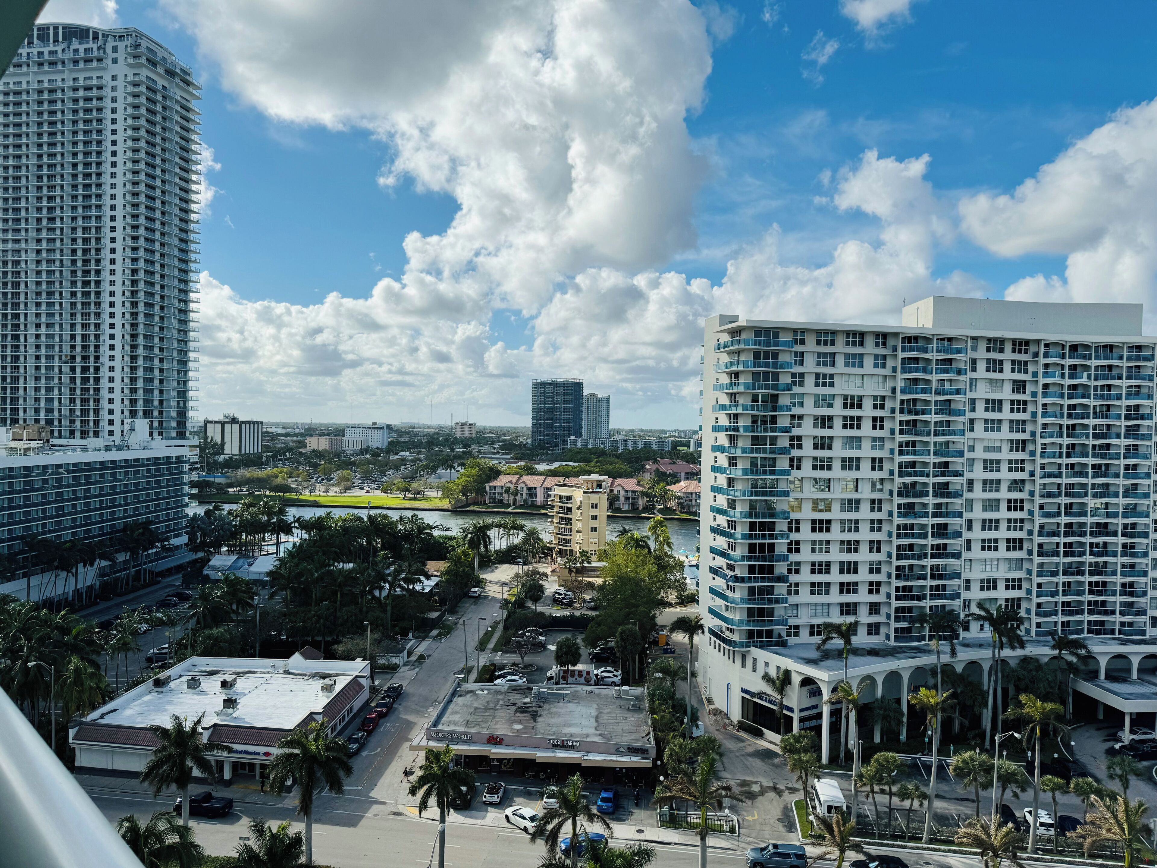 A high-rise hotel with multiple balconies, a parking lot, and a view of a cityscape with other buildings and a river.