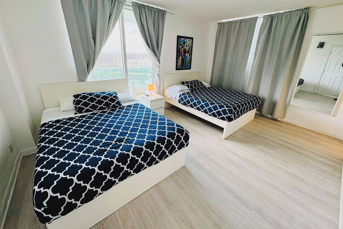 A hotel room with two beds, a nightstand, a lamp, and a painting on the wall.