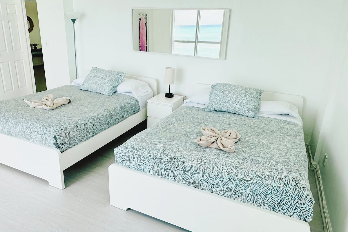 Two twin beds with matching blue patterned bedding and white headboards, a bedside table with a lamp, and a framed artwork above the beds.