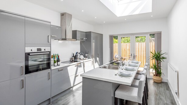 A modern kitchen with a central island, built-in oven, and a large window overlooking a wooden deck. - Beautiful Apartment in Central Neighbourhood (Cardiff)