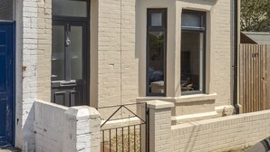 A two-story white brick house with a blue door, a small porch, and a black car parked in front. - Beautiful Apartment in Central Neighbourhood (Cardiff)