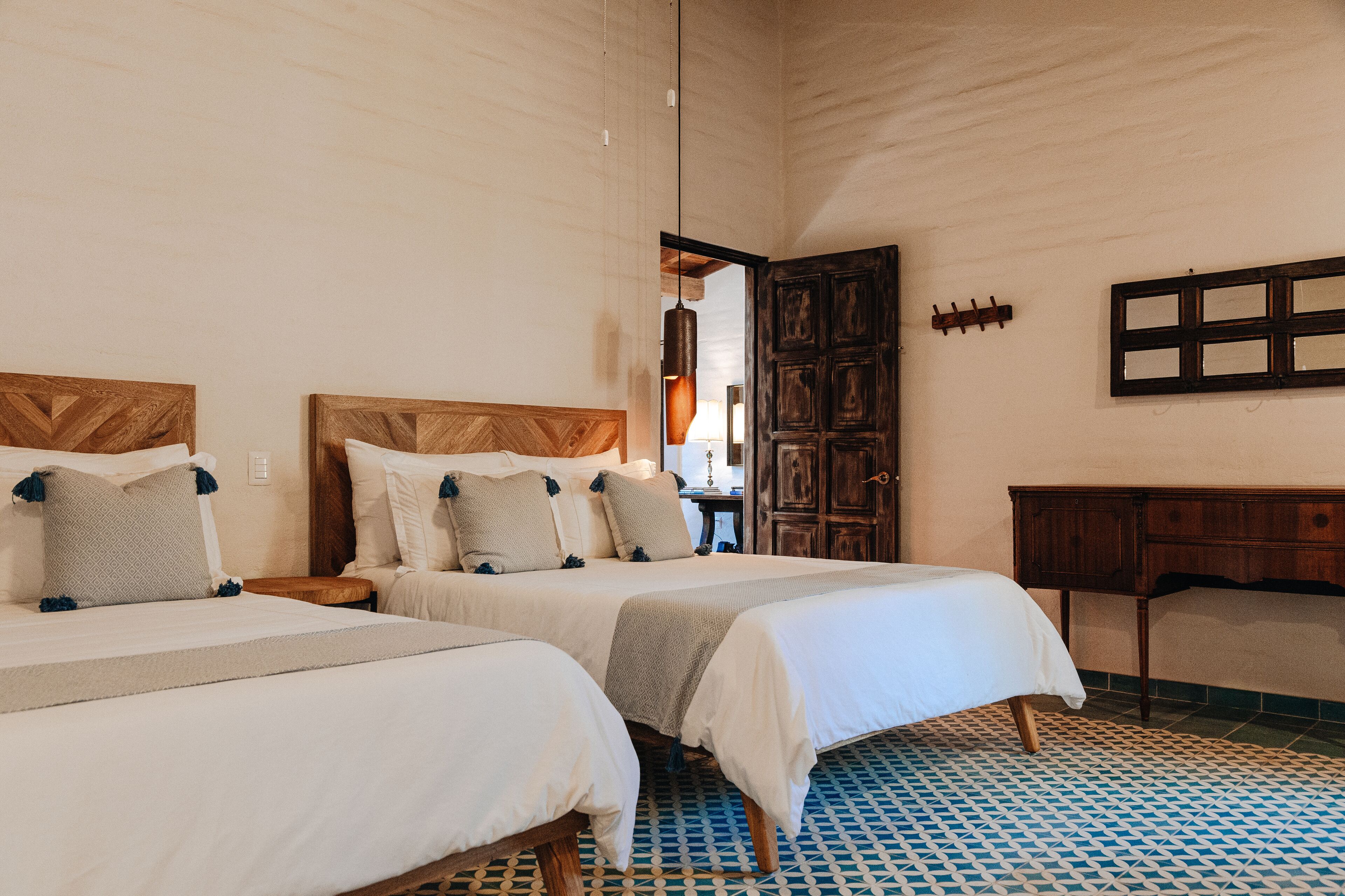 A bedroom with two beds, wooden headboards, a wooden wardrobe, and a patterned floor.