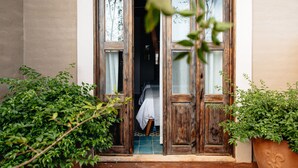 Una porta in legno con pannelli di vetro, un pavimento piastrellato e un letto con un lenzuolo bianco visibile all'interno.