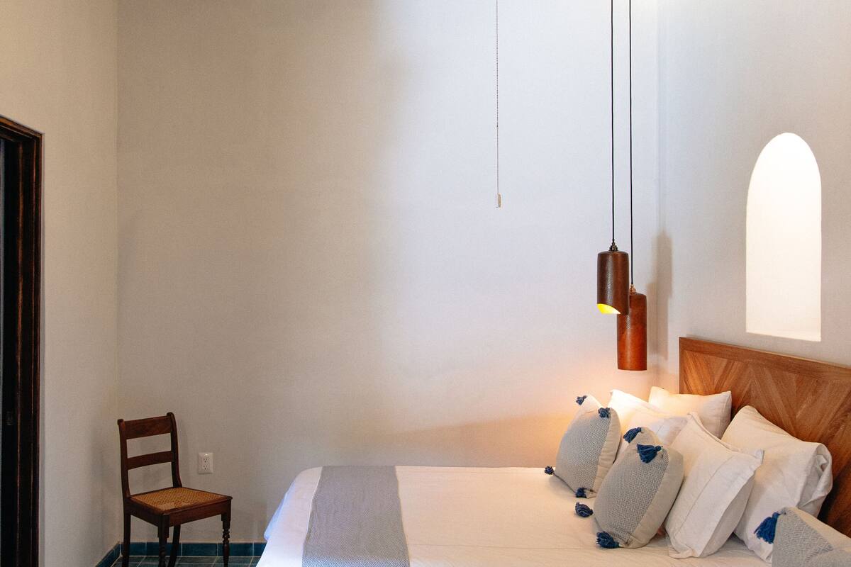 A bedroom with two beds, a ceiling fan, a wooden chair, and a hanging pendant light.