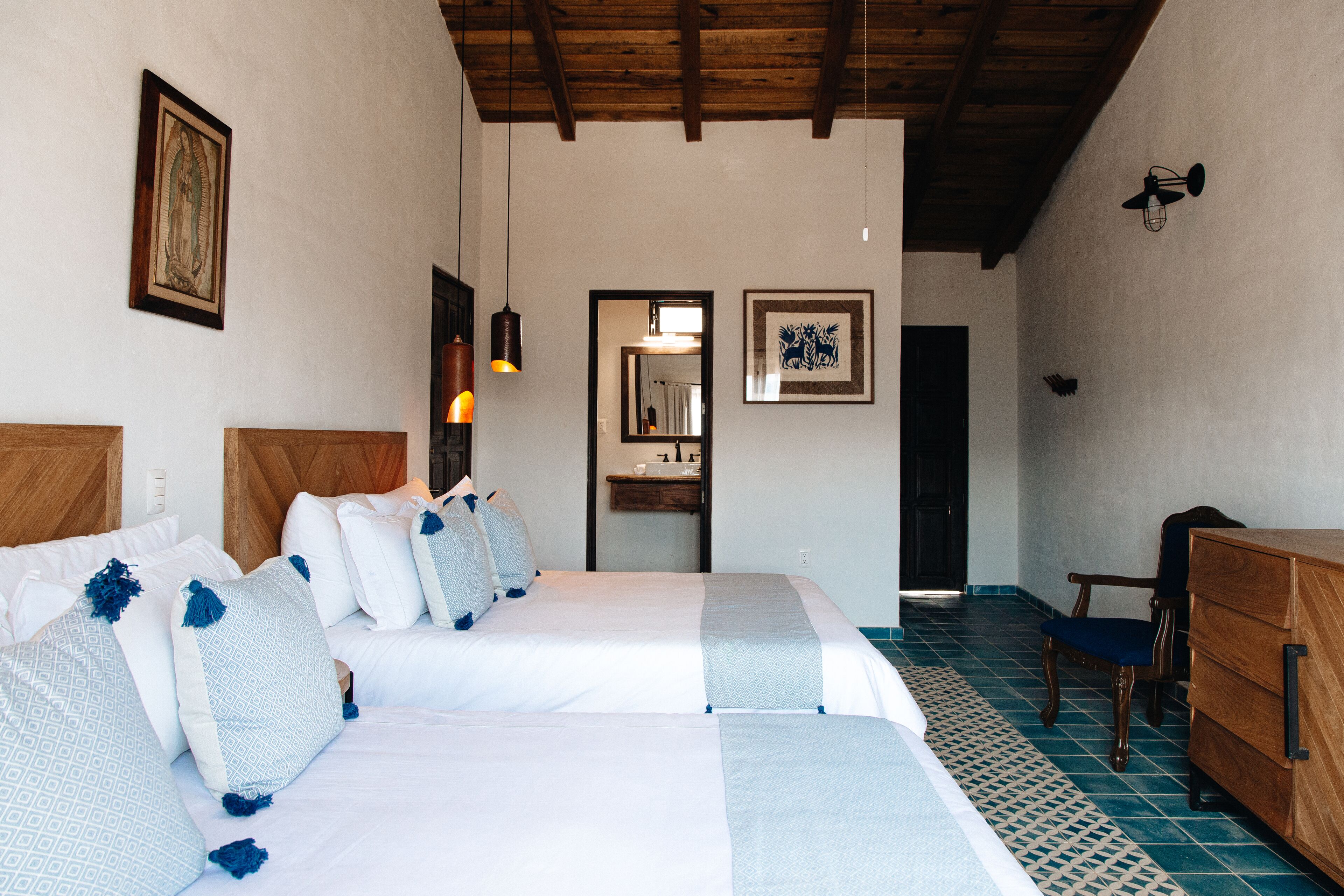 A hotel room with two beds, a wooden dresser, a chair, and a bathroom visible through an open door.