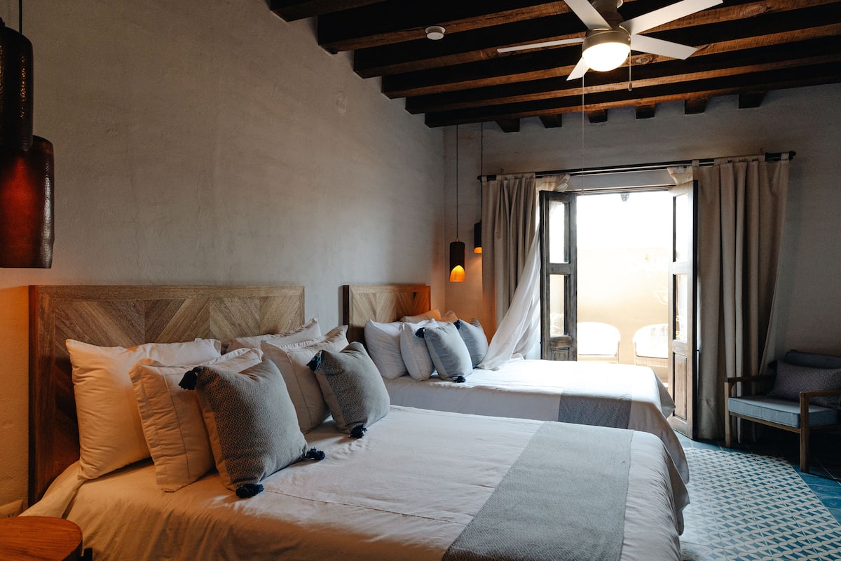 A hotel room with a large bed, a wooden ceiling, and a window with curtains.