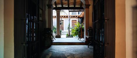 An arched doorway leading to a courtyard with a tiled floor, columns, and a wooden ceiling.
