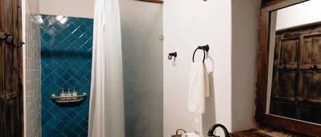 Un baño con un lavamanos blanco, una puerta de madera, un muro con azulejos azules y un espejo con marco de madera.