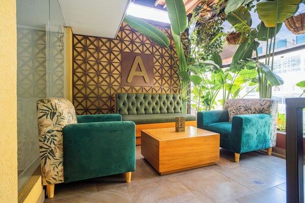 Un área de estar moderna con sofás verdes, una mesa de centro de madera y una pared con estampado geométrico que incluye una 'A' grande.