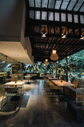 Un espacio interior con mesas y sillas, un muro de cristal y lámparas colgantes.