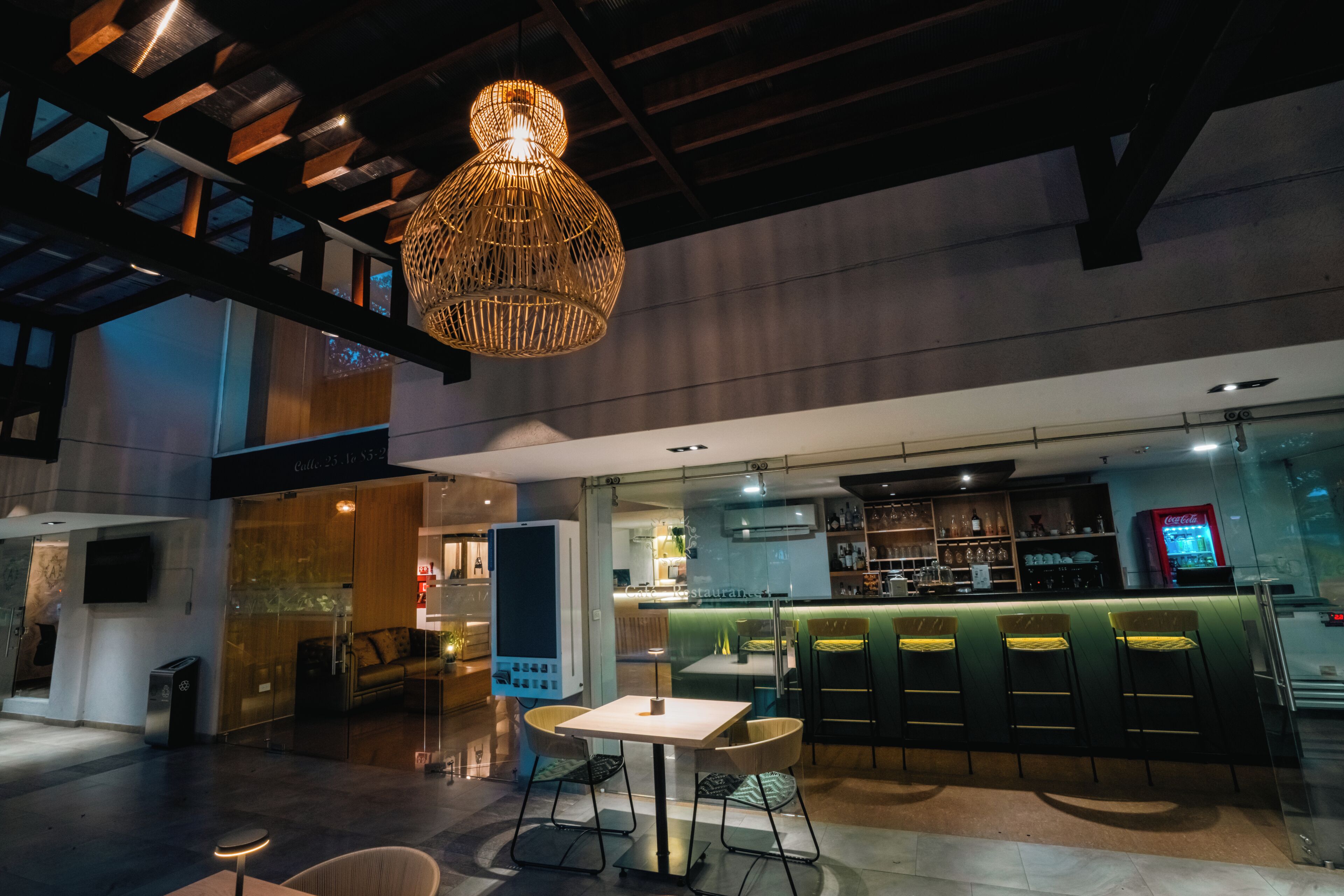 Zona de bar moderna con techo alto, lámpara colgante y disposición de asientos con taburetes.