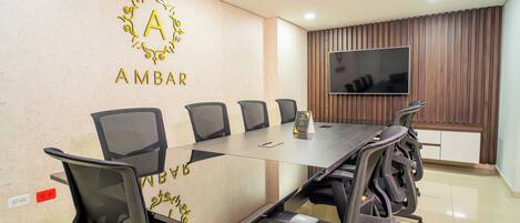 A conference room with a long table, six chairs, a flat-screen TV, and a wall-mounted logo.