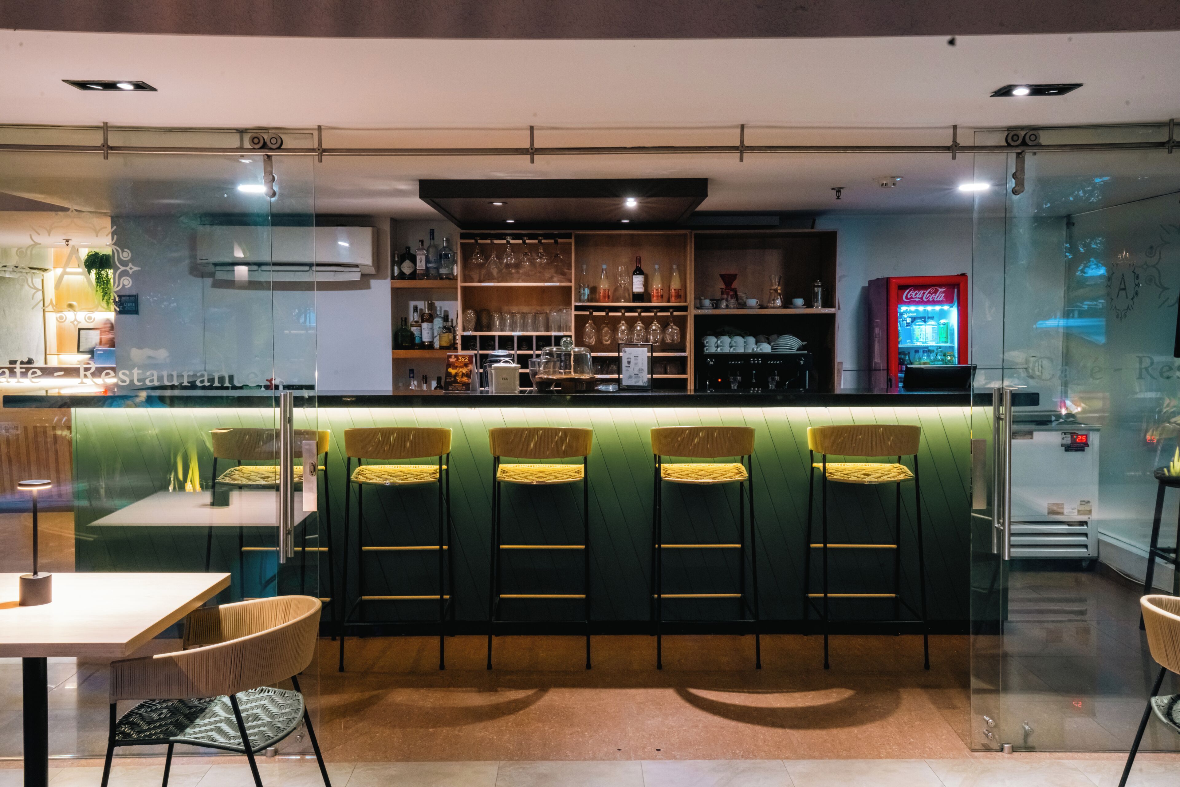 A bar area with a counter, bar stools, shelves with bottles, and a Coca-Cola machine.