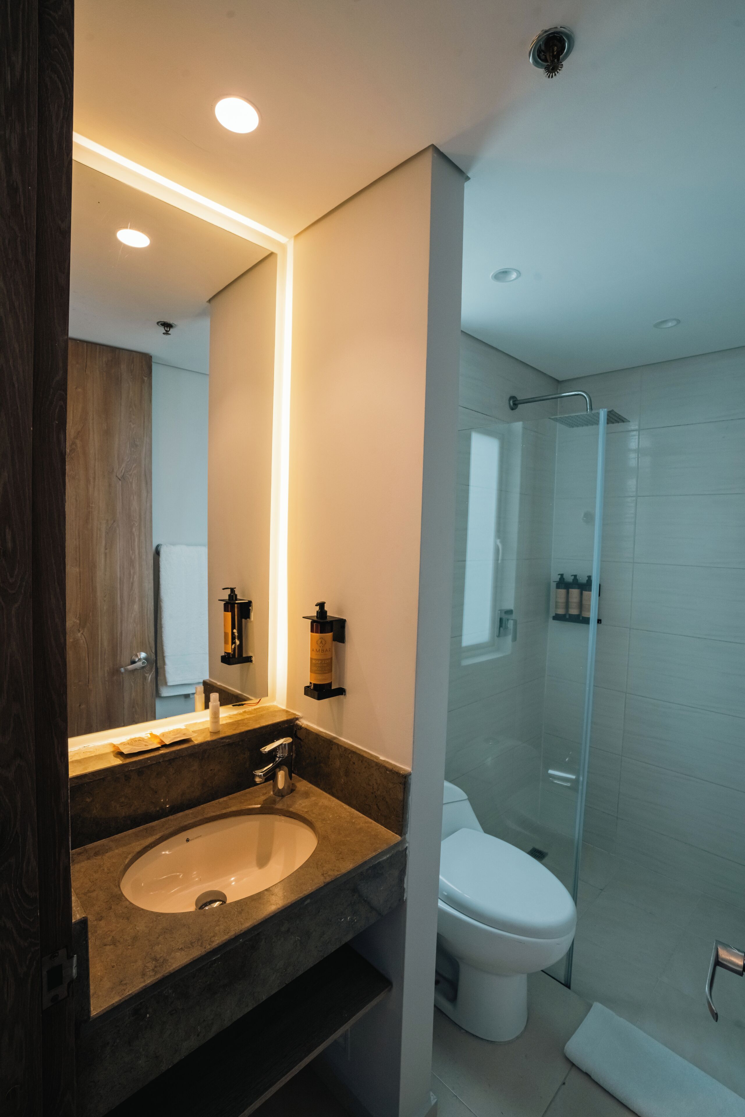 A modern bathroom with a marble sink, a toilet, a glass shower enclosure, and a large mirror.