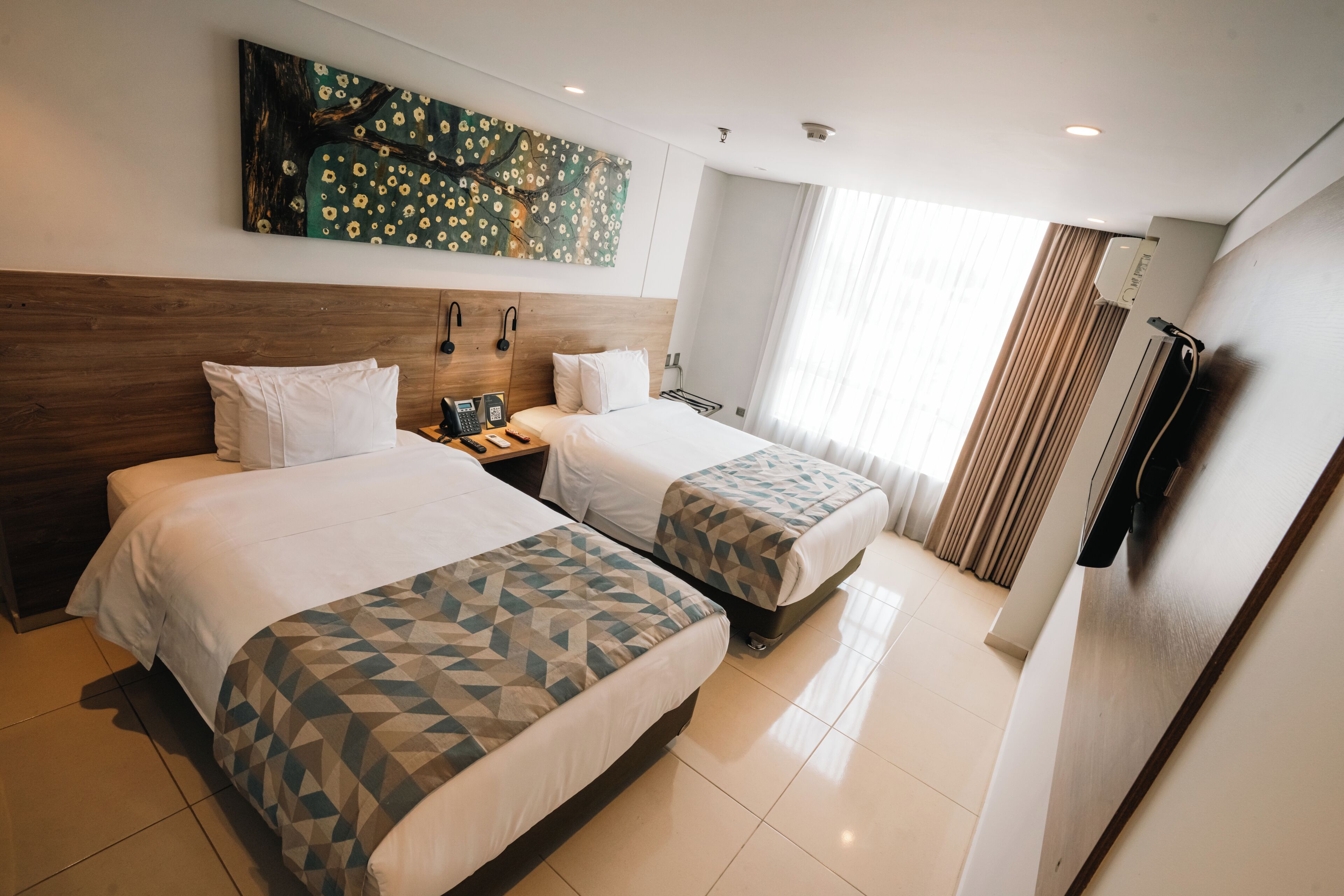 A hotel room with two beds, a large painting on the wall, a telephone, and a window with curtains.