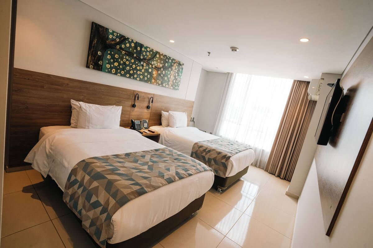 A hotel room with two beds, a painting on the wall, a telephone, and a TV mounted on the wall.