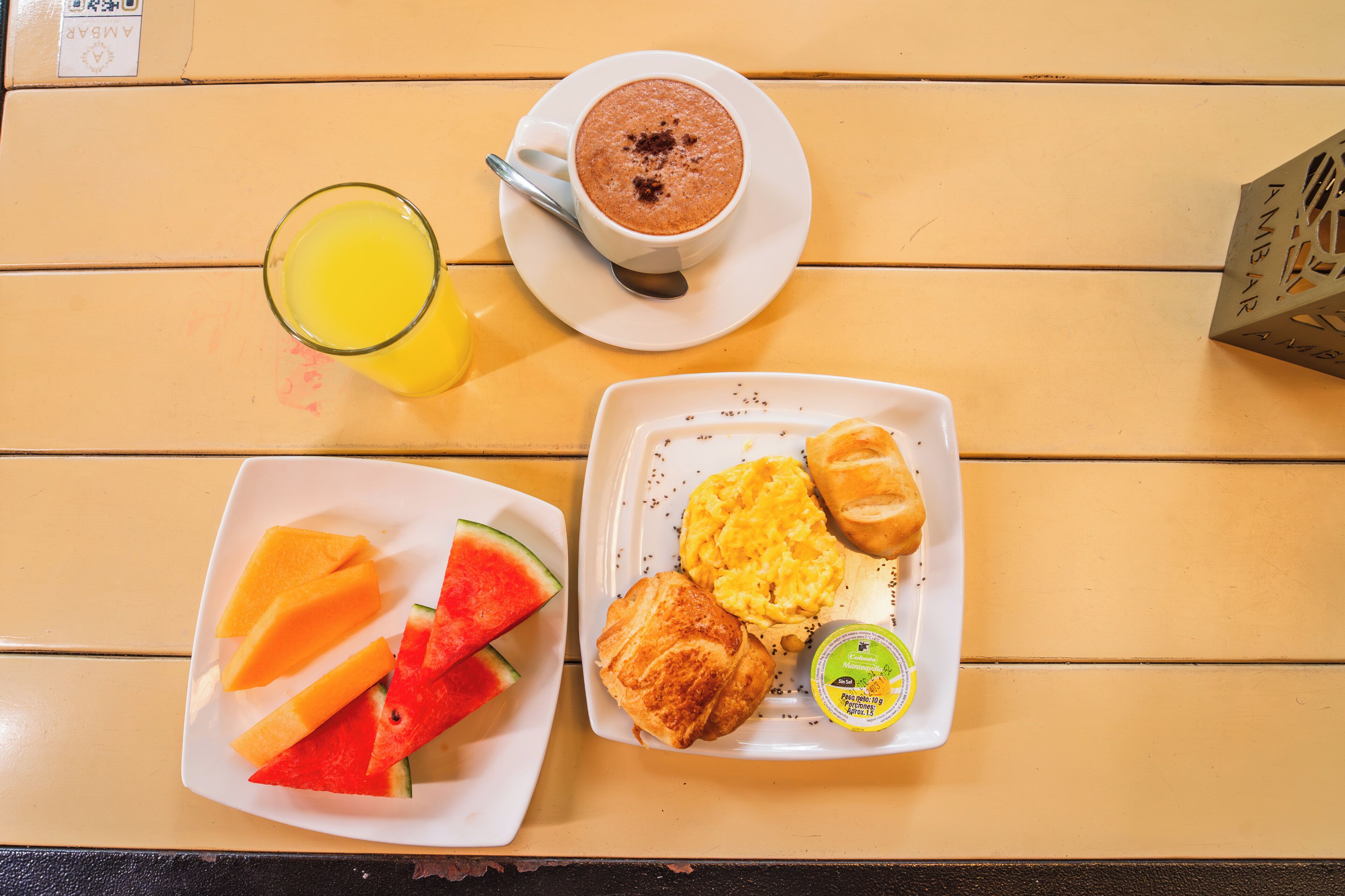 Een ontbijfwagen met een kop koffie, een glas sinaasappelsap en een bord met croissants, roerei en watermeloen.