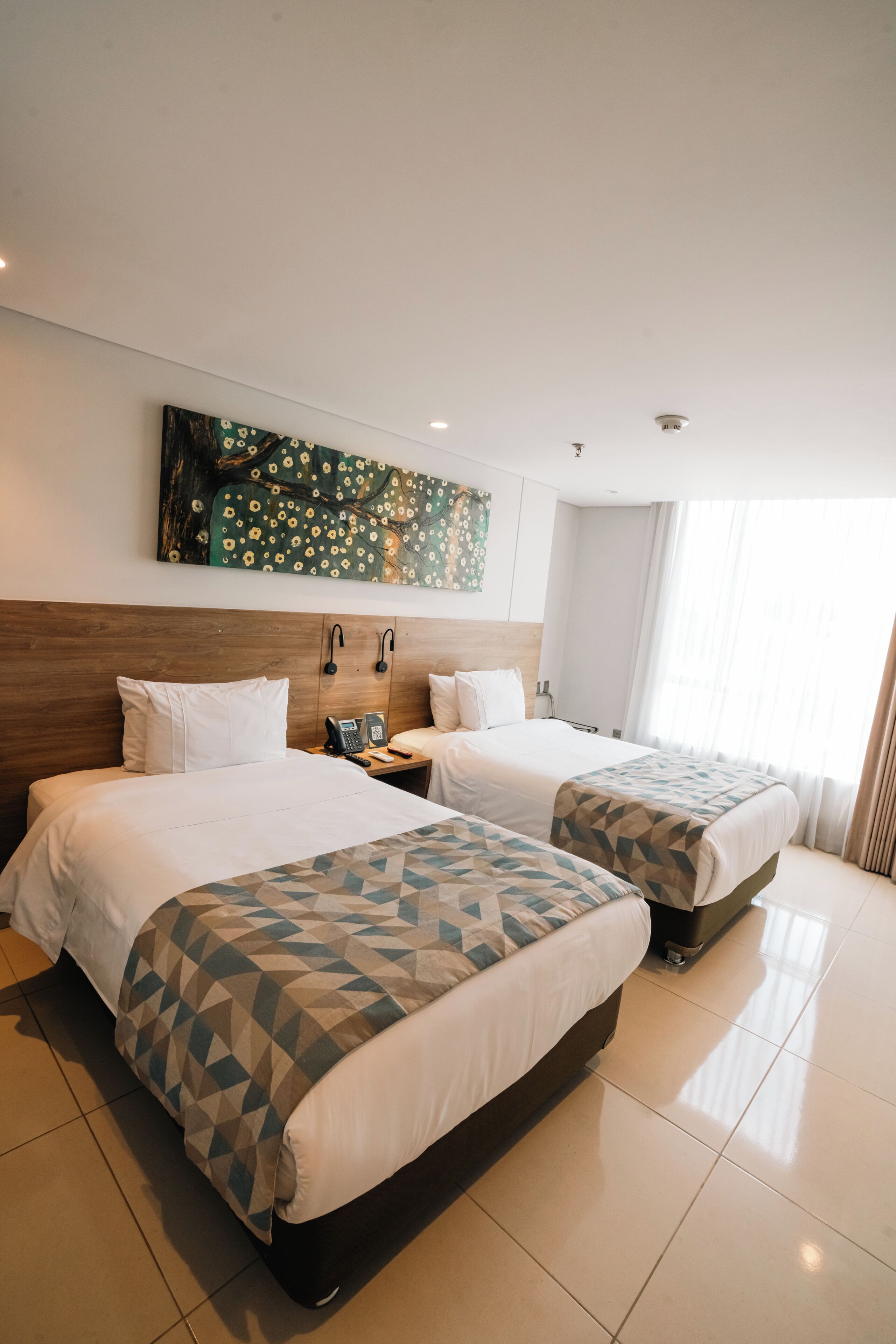 A hotel room with two beds, a wooden headboard, a telephone, and a painting on the wall.