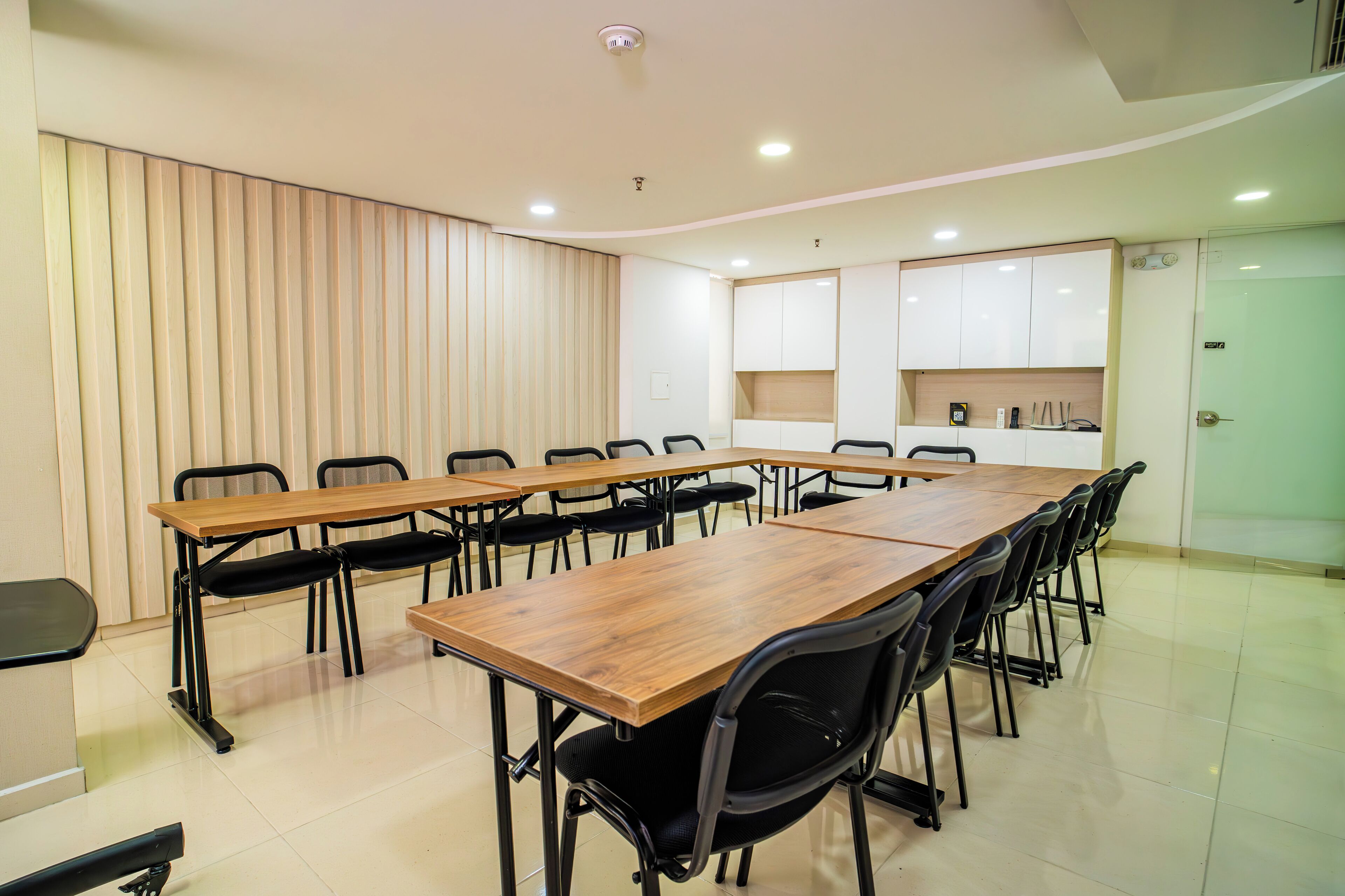 Un salón de conferencias con una larga mesa de madera, sillas negras y armarios blancos al fondo.