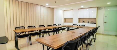 Un salón de conferencias con una larga mesa de madera, sillas negras y armarios blancos al fondo.