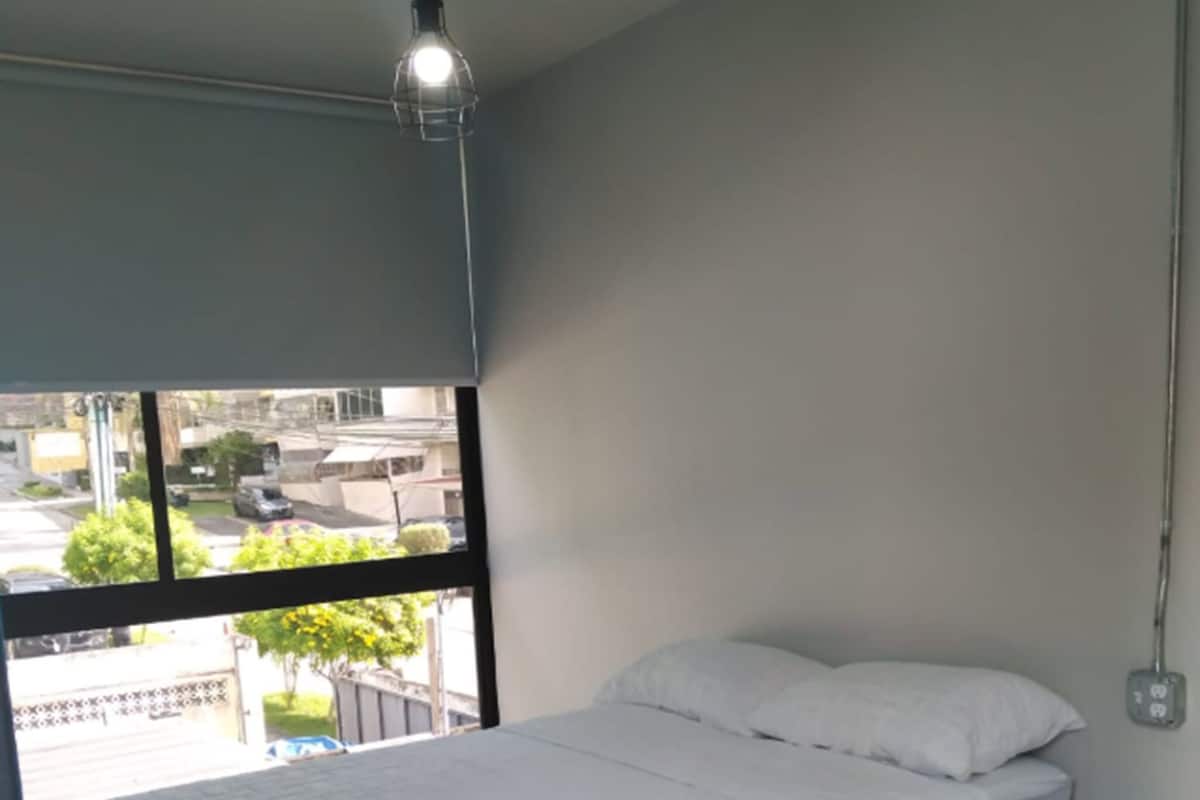 A bedroom with a bed, a window, and a hanging light fixture.