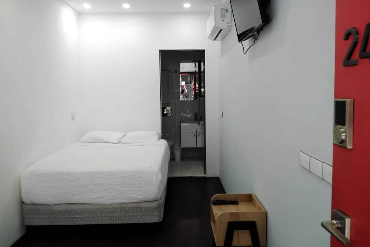 A modern hotel room with a bed, a TV mounted on the wall, a red door, and a small wooden stool.