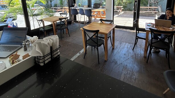 A modern cafe with large windows, wooden tables, and chairs. - Nomada Container Hotel Panama City (Panama City)