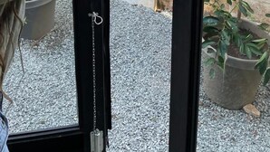 A person opening a sliding glass door to a courtyard with a potted plant and gravel ground. - Nomada Container Hotel Panama City (Panama City)