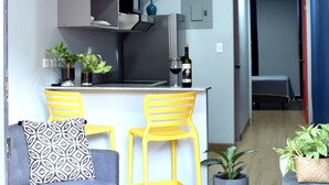 A modern living space with a grey sofa, yellow chairs, a kitchen area with a TV, and potted plants. - Nomada Container Hotel Panama City (Panama City)