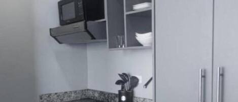 A compact kitchen with a microwave, a sink, and a utensil holder.