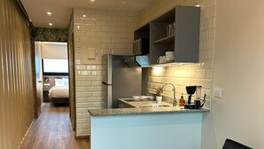 A modern kitchen with a central island, a built-in microwave, and a dark-colored sofa in a living area. - Nomada Container Hotel Panama City (Panama City)