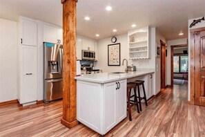 A modern kitchen with white cabinetry, stainless steel appliances, and a wooden island with bar stools. - Recently remodeled! Close to everything in majestic Snowcreek Resort (Mammoth Lakes)