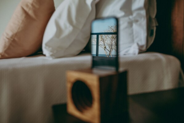 A smartphone on a bedside table with a view of a tree through a window. - Barracuda Hotel & Villas (Itacaré)