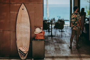 Una tabla de surf de madera apoyada contra una pared, una maleta y un sombrero encima de la maleta.