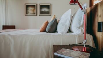 Una cama bien hecha con almohadas, una lámpara de escritorio roja y un libro en una mesita de noche en una habitación con paredes de madera y cuadros en la pared.