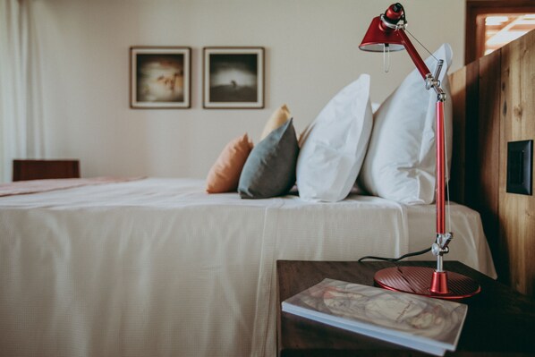 Una cama bien hecha con almohadas, una lámpara de escritorio roja y un libro en una mesita de noche en una habitación con paredes de madera y cuadros en la pared.