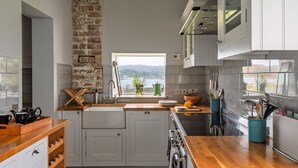 A modern kitchen with white cabinets, a brick accent wall, a large window with a view of hills, and a wooden countertop. - Adventure awaits you on your very own private island off Skye! (Isle of Skye)