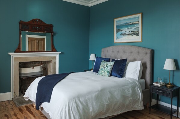A bedroom with a bed, a nightstand, a lamp, a painting, and a fireplace.