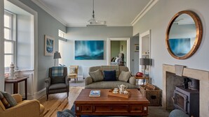 A cozy living room with a fireplace, a sofa, a coffee table, and a large painting on the wall. - Adventure awaits you on your very own private island off Skye! (Isle of Skye)