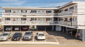 A multi-story motel with a parking lot, multiple balconies with flower baskets, and a sign advertising beach houses for rent. - Nautical Motel (Hampton)